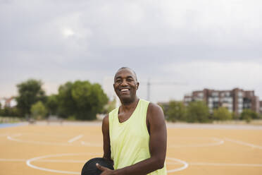 Smiling mature man with basketball standing at sports court - JCCMF07201