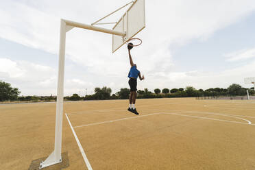 Young man dunking basketball in hoop at sports court - JCCMF07218