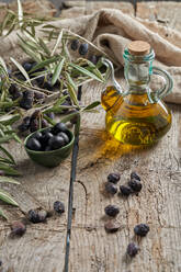 From above black olives and jug of oil placed near fresh tree twigs on wooden table in rustic kitchen - ADSF37551