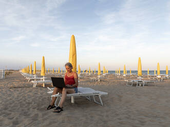 Ältere Geschäftsfrau benutzt Laptop am Strand - FLLF00673