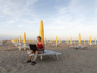 Senior businesswoman using laptop at beach - FLLF00673