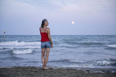 Woman standing at beach with moon over horizon - FLLF00690