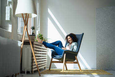 Smiling businesswoman sitting on chair with smart phone at office - JOSEF13029