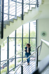 Businesswoman talking on smart phone at staircase in workplace - JOSEF13035