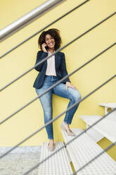 Happy businesswoman talking through smart phone on staircase - JOSEF13038