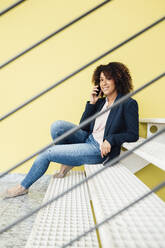 Businesswoman talking through smart phone sitting on steps - JOSEF13039