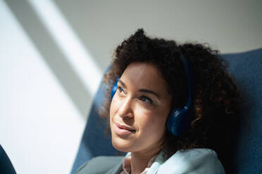 Contemplative businesswoman listening music through wireless headphones - JOSEF13052