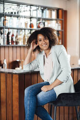 Lächelnde Frau sitzt auf einem Stuhl in einer Bar - JOSEF13053