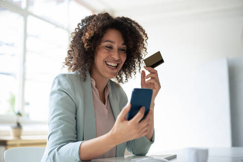 Happy businesswoman doing online payment through smart phone at workplace - JOSEF13057