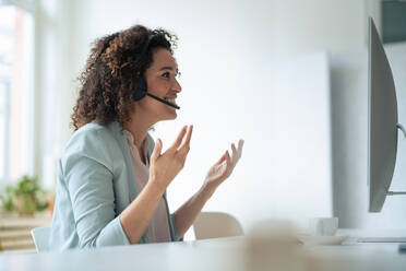 Lächelnde Geschäftsfrau, die durch ein Headset spricht und im Büro gestikuliert - JOSEF13064