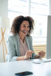 Happy customer service representative discussing through headset at workplace - JOSEF13068