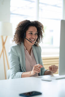 Happy customer service representative discussing through headset at workplace - JOSEF13068