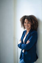 Happy mature businesswoman with arms crossed leaning on wall - JOSEF13077