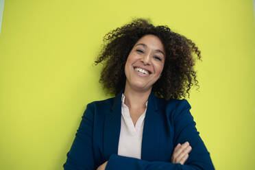 Happy businesswoman with arms crossed in front of wall - JOSEF13105