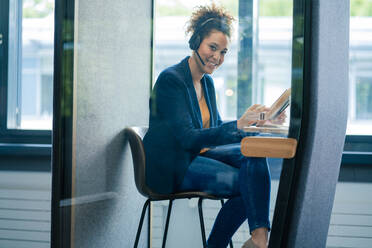 Smiling businesswoman with tablet PC sitting in soundproof cabin at office - JOSEF13121