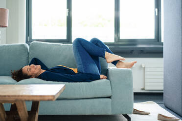 Lächelnde Geschäftsfrau entspannt sich auf dem Sofa in der Pause im Büro - JOSEF13128