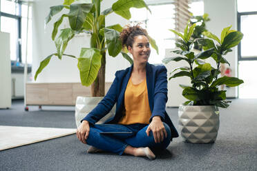 Businesswoman with tablet PC sitting by potted plants at workplace - JOSEF13135