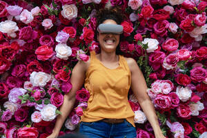 Fröhliche Frau mit VR-Brille auf Blumen liegend - JOSEF13140