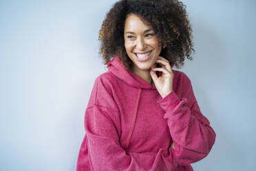 Happy woman wearing hooded shirt in front of white wall - JOSEF13143