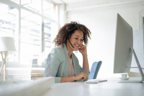 Happy businesswoman working on computer at workplace - JOSEF13154