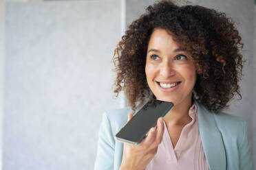 Lächelnde Geschäftsfrau, die eine Voicemail über ihr Smartphone sendet - JOSEF13162