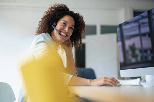 Businesswoman wearing headset laughing in office - JOSEF13192