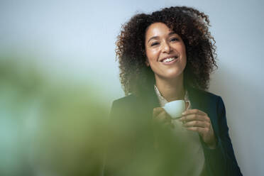Smiling businesswoman having coffee in front of wall - JOSEF13201