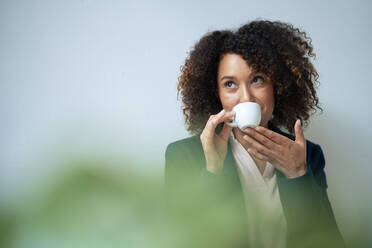 Mature businesswoman drinking coffee in front of wall - JOSEF13202