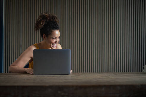 Glückliche Geschäftsfrau mit Laptop auf einem Tisch vor einer Wand - JOSEF13215