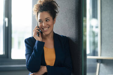 Happy businesswoman talking on mobile phone in office - JOSEF13224