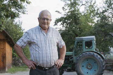 Älterer Landwirt mit den Händen in den Hüften vor einem Traktor stehend - OSF00906