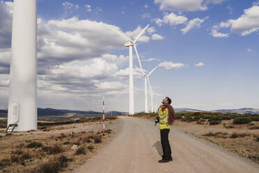 Techniker mit Seil steht auf der Straße und schaut auf eine Turbine im Windpark - EBBF06296