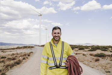 Lächelnder Techniker mit Seil im Windpark - EBBF06301