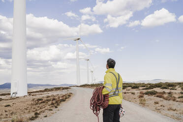 Engineer with rope looking at wind turbines at wind farm - EBBF06302