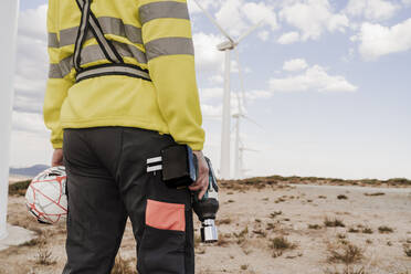 Techniker mit Arbeitsgerät und Helm im Windpark stehend - EBBF06305