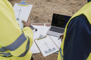 Ingenieur mit Klemmbrett bei einem Kollegen am Schreibtisch in einem Windpark - EBBF06309