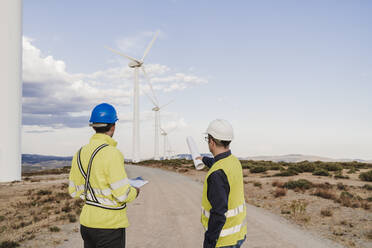 Technicians discussing on road looking at wind turbines at wind farm - EBBF06336