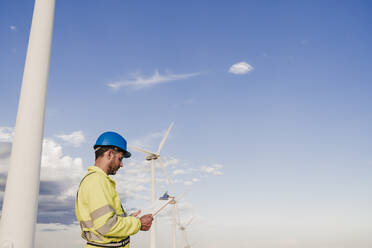 Engineer wearing hardhat working by wind turbines - EBBF06338