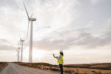 Ingenieur betrachtet die Turbinen eines Windparks bei Sonnenuntergang - EBBF06358