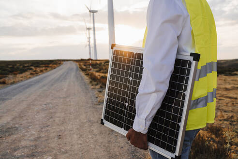 Ingenieur hält Solarpanel in Windpark bei Sonnenuntergang - EBBF06360