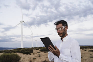 Engineer wearing protective glasses using tablet PC at wind farm - EBBF06379