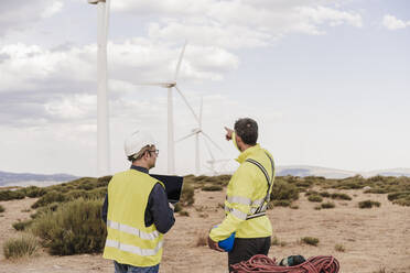 Engineer pointing by colleague standing at wind farm - EBBF06393