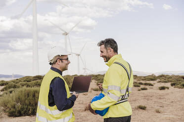 Lächelnde ältere Kollegen diskutieren im Windpark - EBBF06396