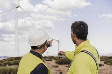 Engineers discussing over wind turbine model at wind farm - EBBF06397