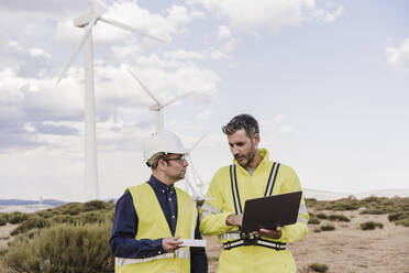 Ingenieur mit Laptop bespricht sich mit einem Kollegen im Windpark - EBBF06398
