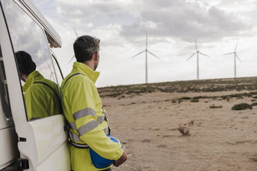 Älterer Techniker betrachtet Turbinen, die an einen Lieferwagen im Windpark gelehnt sind - EBBF06399