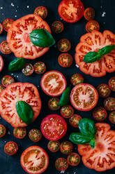 Von oben halbierte Tomaten auf dem Tisch mit Basilikumblättern - ADSF37661