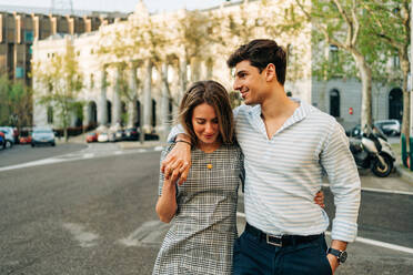 Smiling couple in trendy clothes standing in city street and embracing with love - ADSF37673