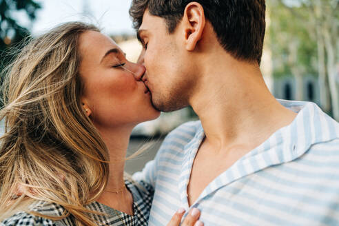 Glückliches Paar in trendiger Kleidung stehen in der Stadt Straße und küssen einander mit Liebe - ADSF37674