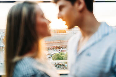 Gentle loving couple embracing and looking at each other in rooftop restaurant during romantic date at sunset in summer - ADSF37677